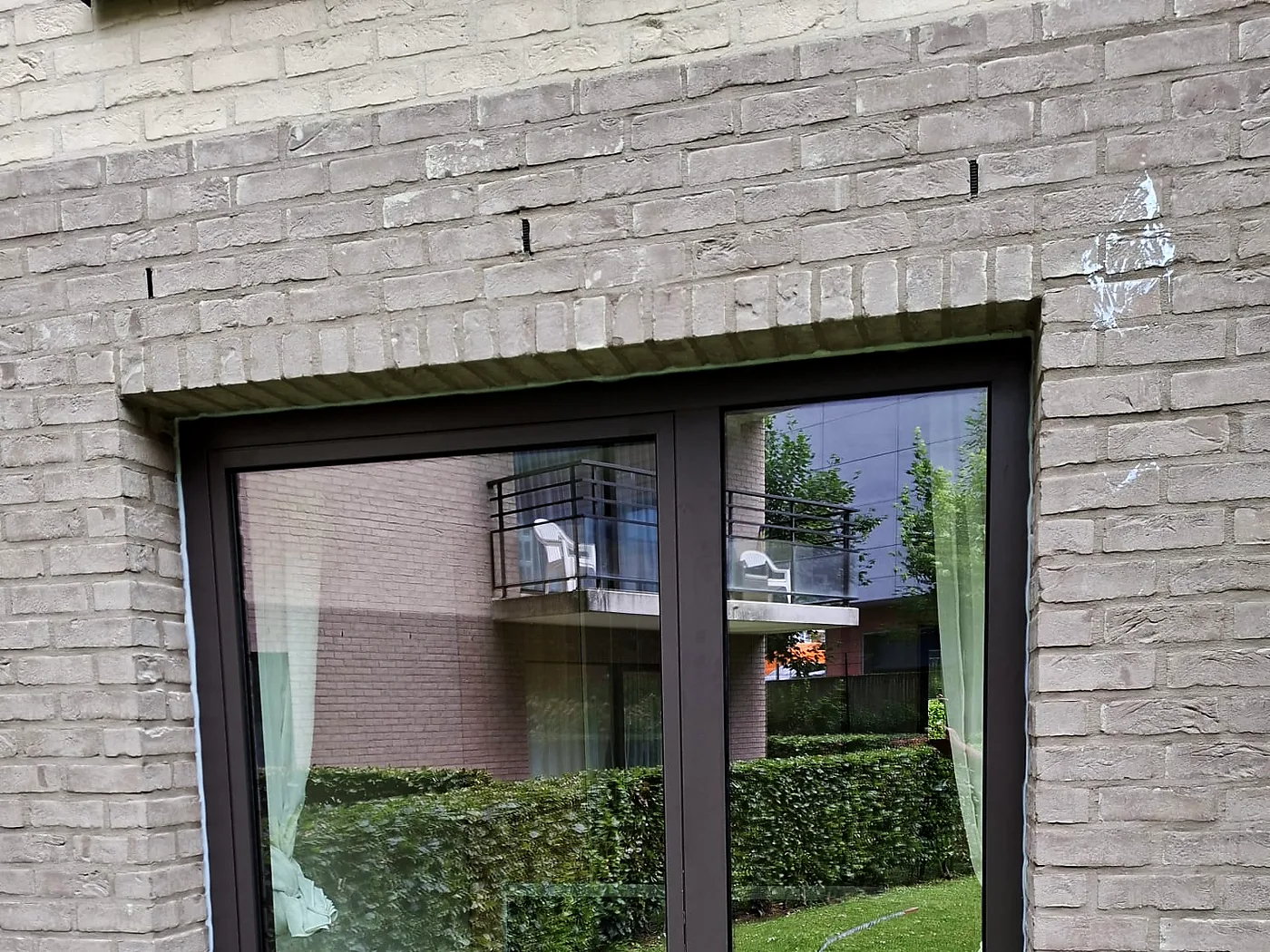 Baie coulissante à profilé noir ouvrant sur un jardin bordé d’une haie — réalisation Pulsar Windows