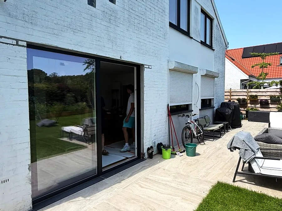Baie coulissante à profilé noir ouvrant sur le jardin d’une maison aux murs blancs — réalisation Pulsar Windows