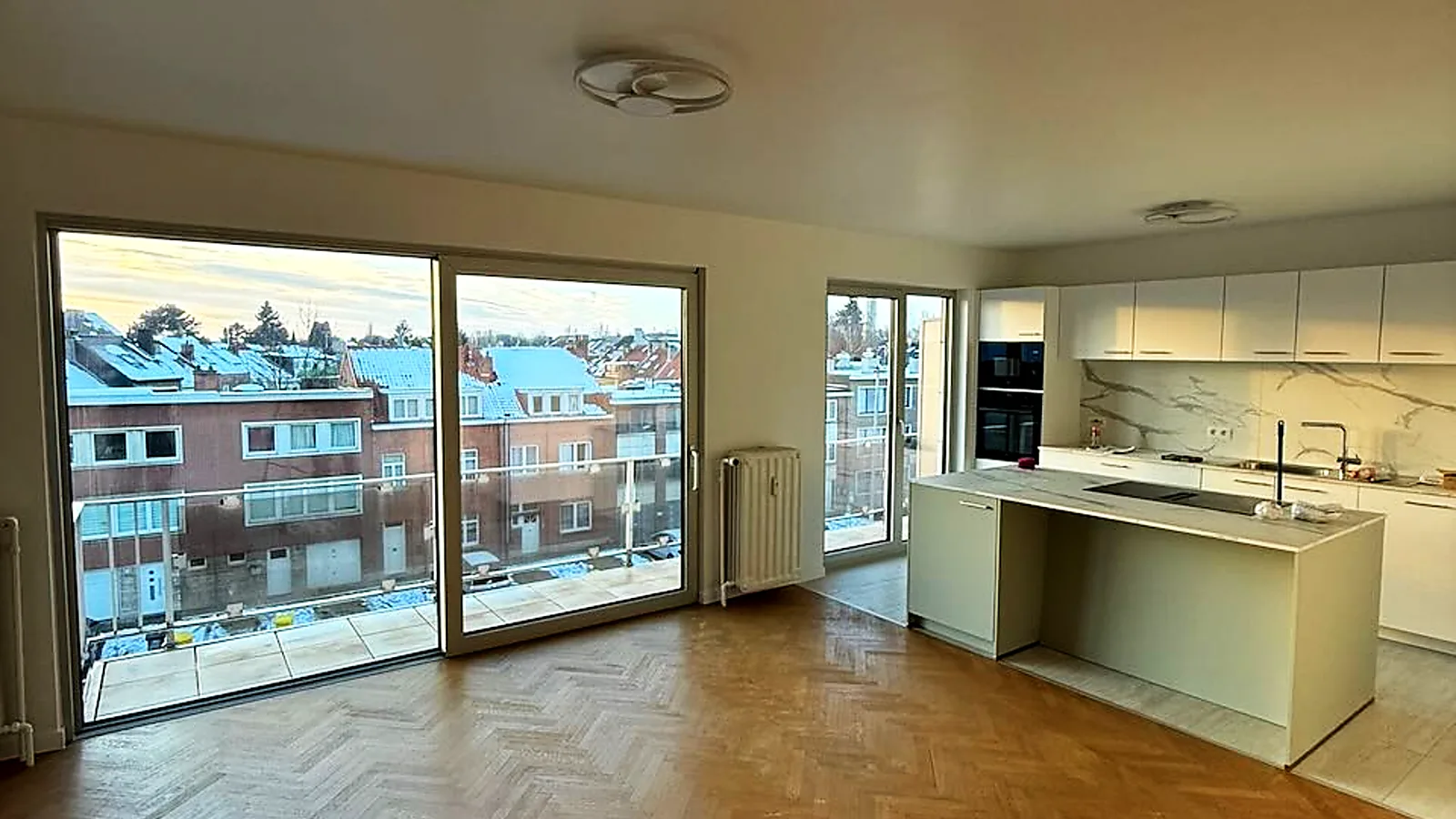 Large black-framed sliding door opening a bright living room onto a terrace, with an open kitchen — a Pulsar Windows project