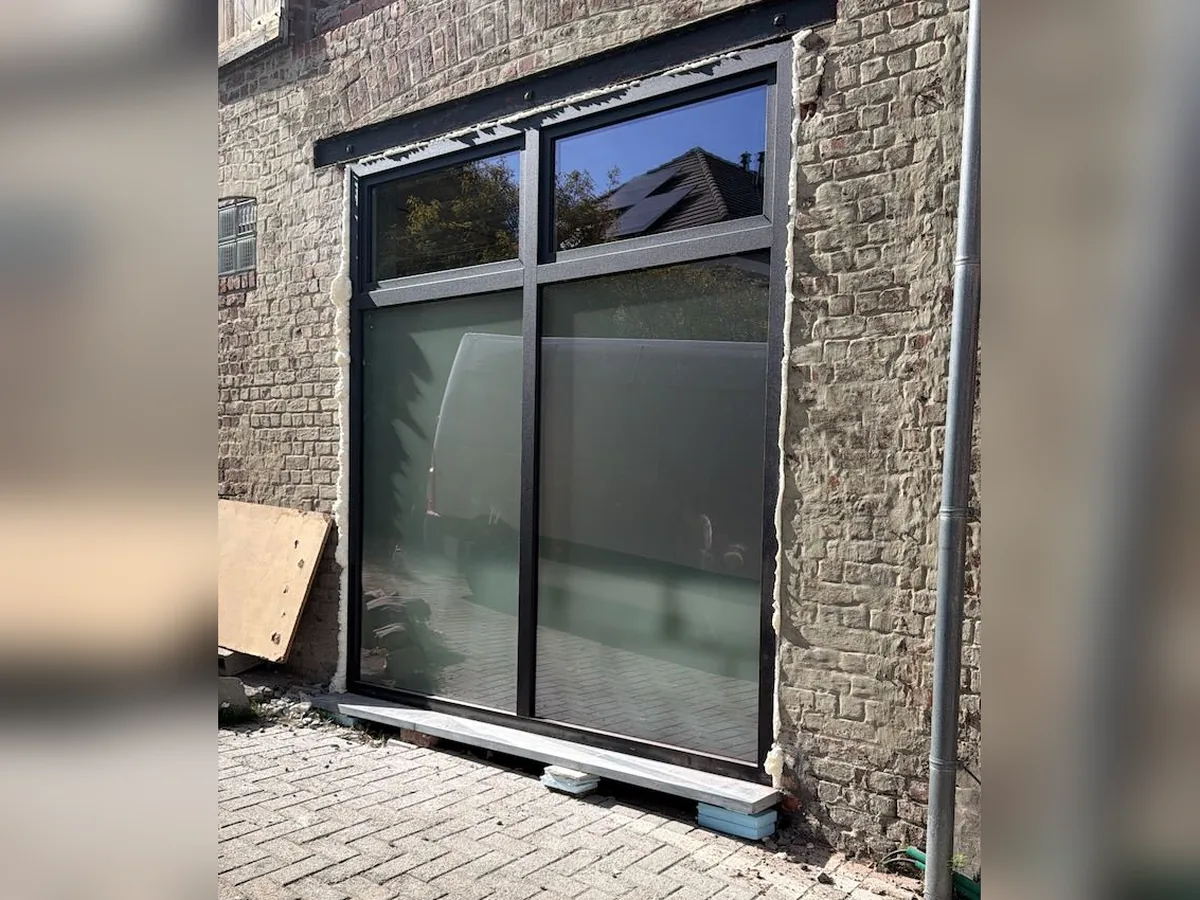 Baie vitrée en aluminium anthracite avec imposte, posée dans l’ouverture d’une ancienne porte de garage sur une façade en briques — réalisation Pulsar Windows