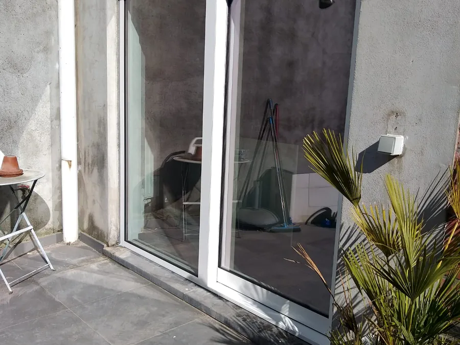Grande baie coulissante à profilé clair ouvrant sur une terrasse, façade en enduit clair — réalisation Pulsar Windows
