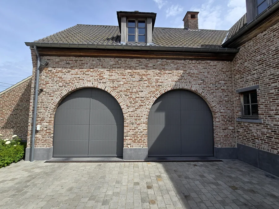 Deux portes de garage cintrées anthracite intégrées à une maison traditionnelle en briques.