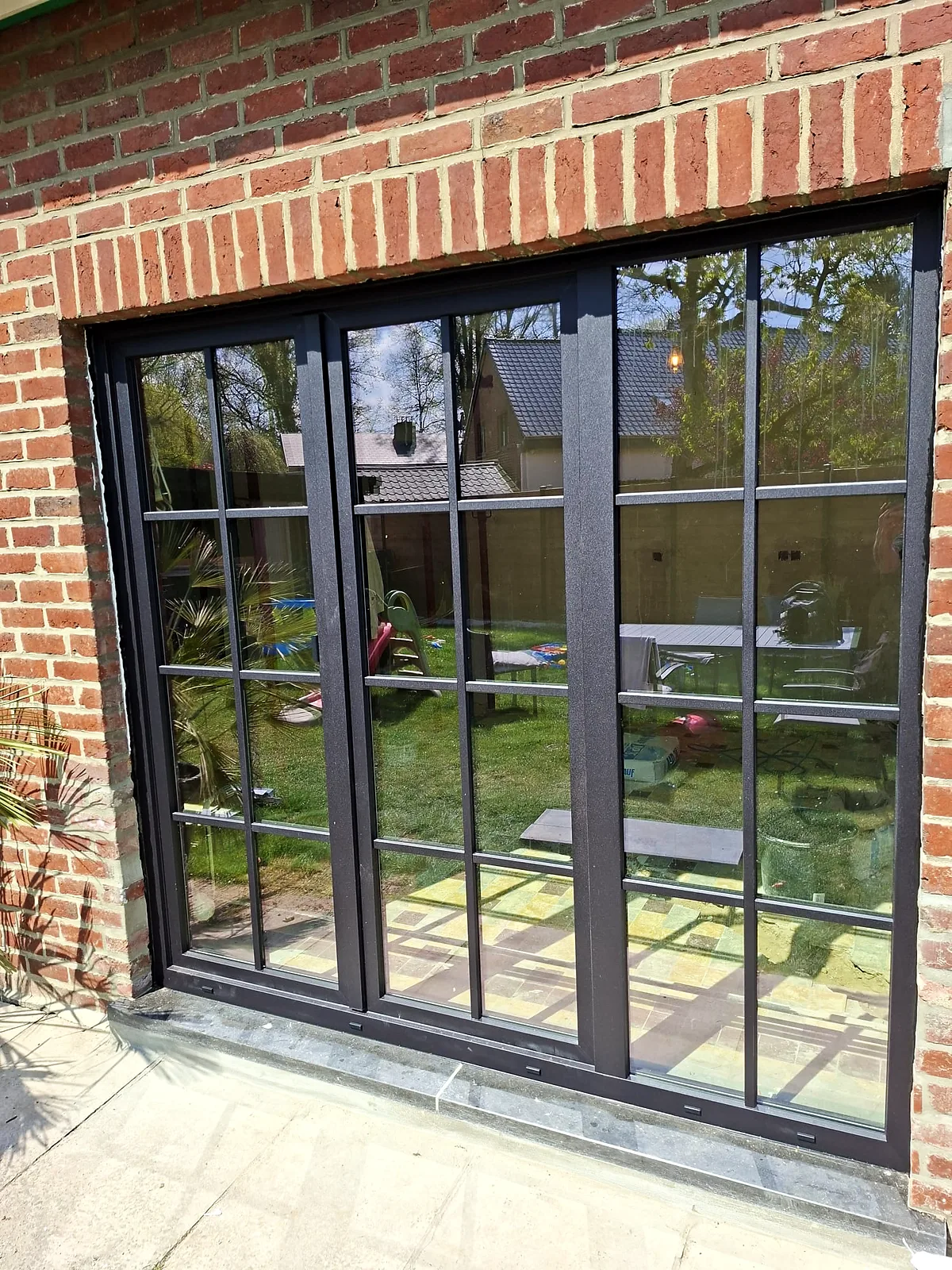 Ensemble de fenêtres à profilé noir et petits bois donnant sur un jardin arboré — réalisation Pulsar Windows