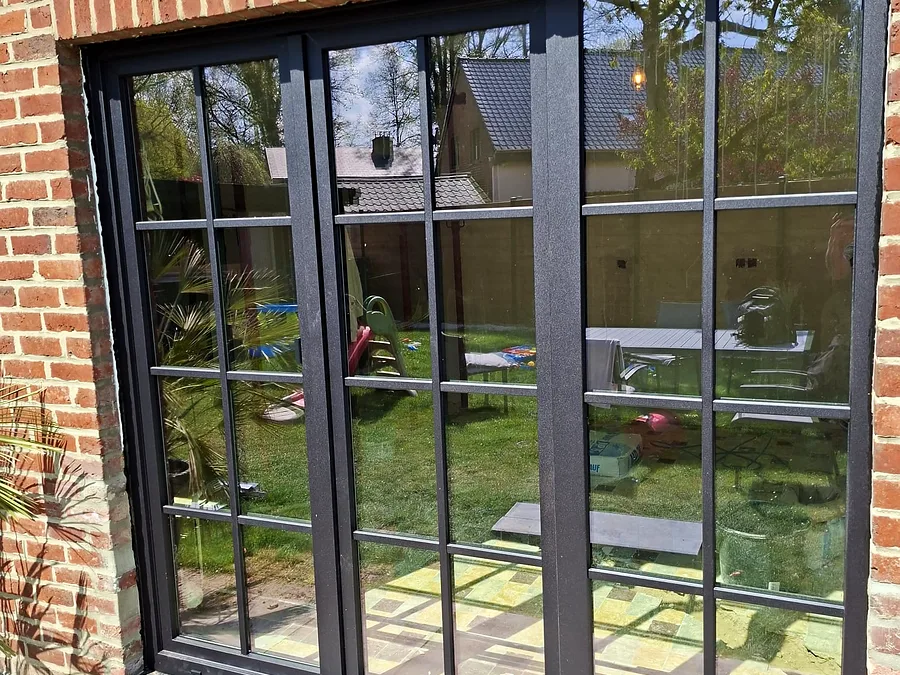 A set of black-framed windows with glazing bars overlooking a wooded garden — a Pulsar Windows project