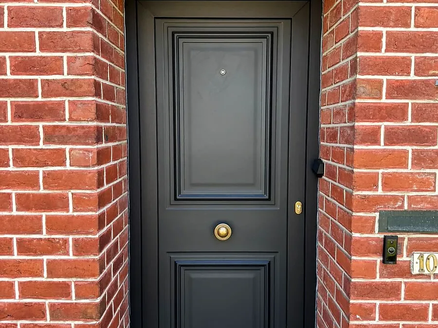 Anthracite entrance door with moulded panels and a brass knob, framed by a red-brick arch — a Pulsar Windows project