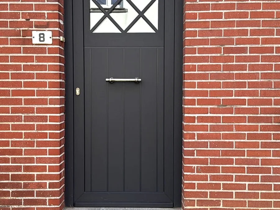 Porte d’entrée anthracite avec vitrage décoratif à losanges sur une façade en briques rouges.