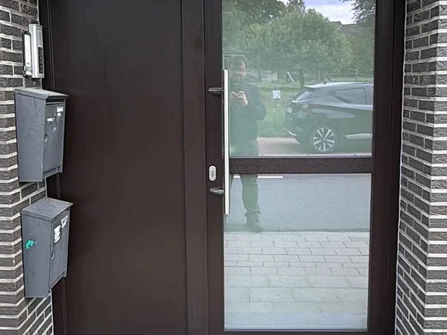 Porte d’entrée brune contemporaine avec grand panneau vitré latéral sur une façade en briques.