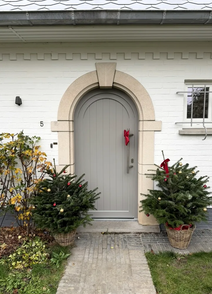 Porte d’entrée cintrée gris clair intégrée dans un encadrement en pierre sur une façade blanche.