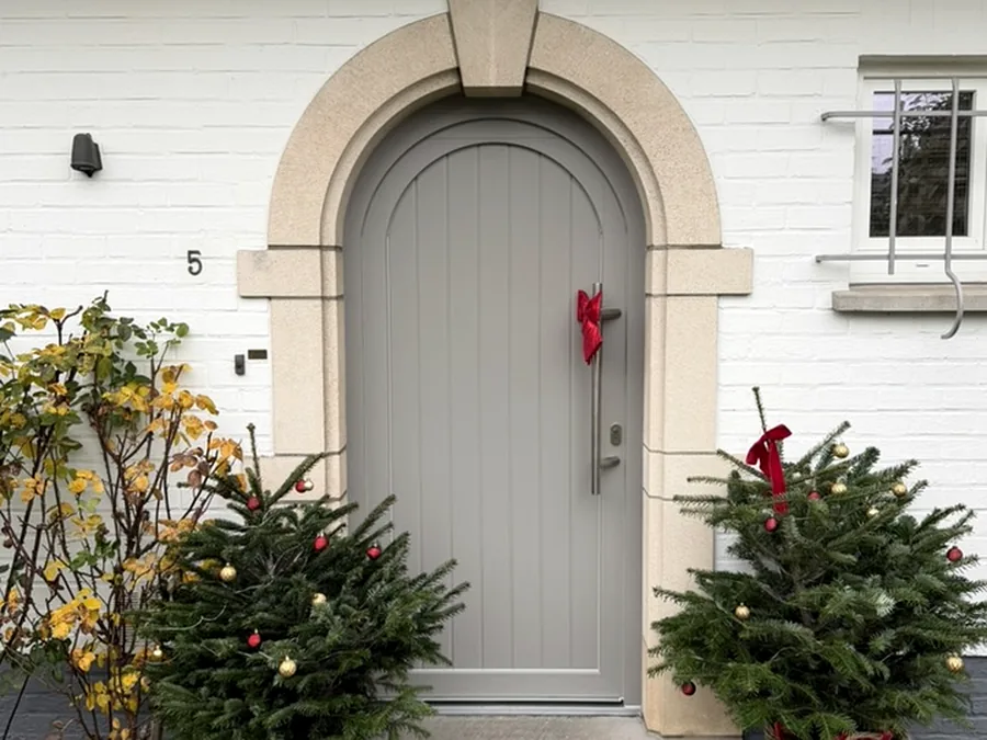 Porte d’entrée cintrée gris clair intégrée dans un encadrement en pierre sur une façade blanche.