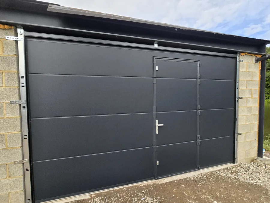 Porte de garage sectionnelle anthracite avec portillon intégré, installée sur une annexe résidentielle.