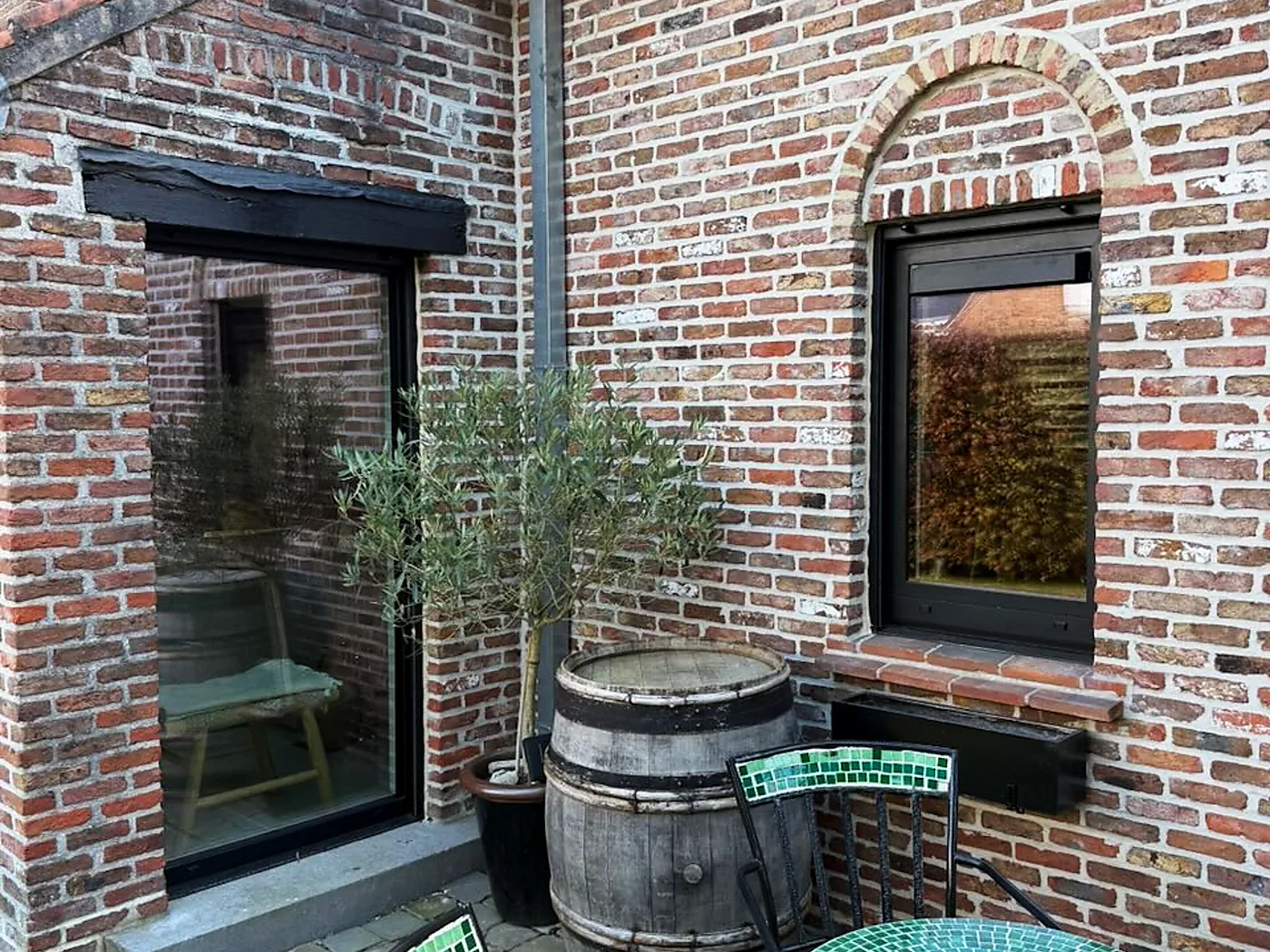 Fenêtres à profilé noir sur une maison en briques rénovée, avec terrasse, olivier et tonneau — réalisation Pulsar Windows