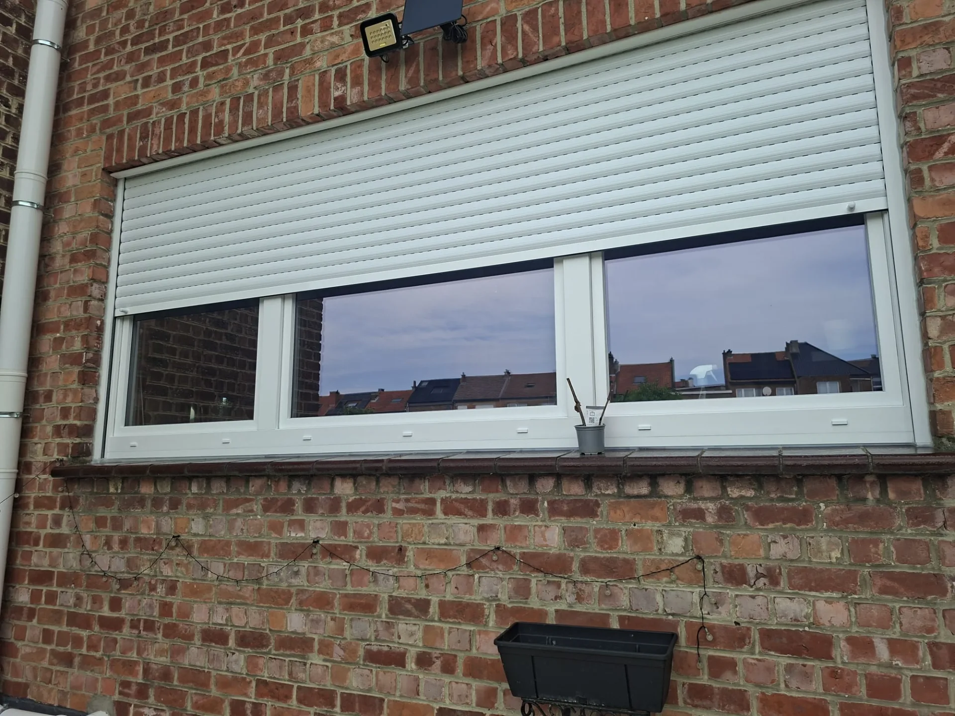 White two-sash PVC window with a white compact-box roller shutter, brick rear façade
